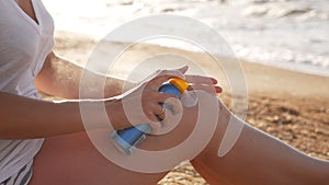 Sunscreen suntan lotion in spray bottle. Young woman in spraying tanning oil on her leg from bottle. Lady is massaging