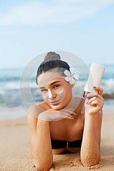 Sunscreen woman applying suntan lotion showing bottle. Beautiful smiling happy woman with suntan cream  lying on beach.