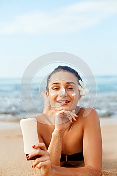 Sunscreen woman applying suntan lotion showing bottle. Beautiful smiling happy woman with suntan cream lying on beach.