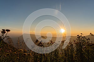 Sunset above horizon line with sun setting down behind mountains