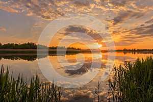 Sunset above the pond or lake with cloudy sky at summer and water reflection