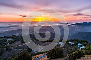 Sunset afterglow over a sea of clouds; winding road descending through rolling hills in the foreground; Mt Hamilton, San Jose,