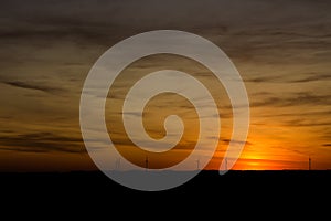 Sunset with afterglow under a cloudy sky with wind turbines on the horizon