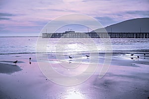 Sunset on the beach in blue and pink colors, long wooden pier and mountains on a horizon