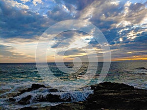 a stunning summer landscape with vast blue ocean water and a gorgeous sunset with powerful clouds and waves rolling into the beach