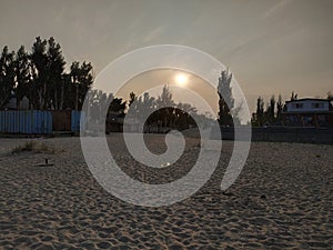 Sunset on the beach. Deserted beach. Rusty fences. The sun behind the clouds falls over the horizon. Sand. The Trees. Coast.