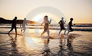 Sunset, beach and friends with freedom, running and having fun in water together on summer vacation. Ocean, silhouette