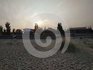 Sunset on the beach. Grass grows on the beach. Deserted beach. Rusty fences. The sun behind the clouds falls over the horizon. San