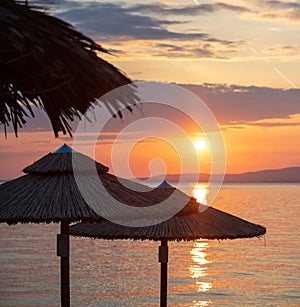 Sunset on the beach. Greece. Straw umbrella silhouette, golden reflection on rippled ocean water