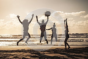 Sunset at the beach with happy group of young people jumping having fun - friends on summer holiday vacation enjoying together in