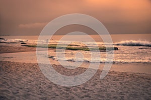 Sunset beach ocean surf waves scenery landscape with dramatic orange sunset sky and fisherman