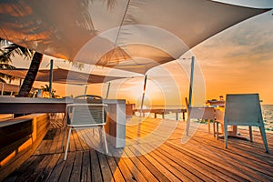 Sunset beach restaurant, sunset light and soft colors on wooden deck with white furniture and sea view