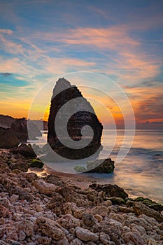 Sunset on the beach. Rock in the ocean. Seascape background. Foreground with stones. Colorful sky. Silky water. Slow shutter speed