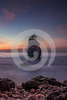 Sunset on the beach. Rock in the ocean. Seascape background. Foreground with stones. Colorful sky. Silky water. Slow shutter speed