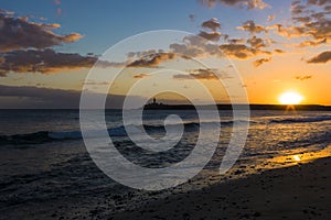 Sunset at the beach with a scenic lighthouse on a cliff.