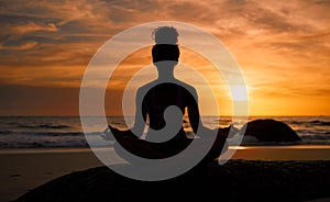 Sunset, beach and silhouette of a woman in a lotus pose while doing a yoga exercise by the sea. Peace, zen and shadow of