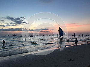 Sunset at the beach in South East Asia, showing silhouttes of people playing in the water and small sailing boats