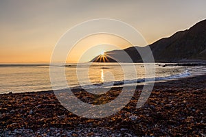 Sunset at the beach of Wellington in New Zealand Nort Island with sun star right above the moutains