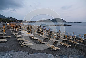 sunset on the beach with yellow sunbeds over the sea and horizon and hills with hotels. Sestri Levante, Liguria, Italy