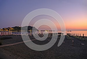 sunset on the beach with yellow sunbeds over the sea and horizon and hills with hotels. Sestri Levante, Liguria, Italy