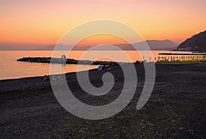 sunset on the beach with yellow sunbeds over the sea and horizon and hills with hotels. Sestri Levante, Liguria, Italy