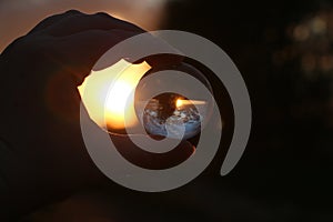 A sunset in a beautiful landscape view through a glass ball held by one hand