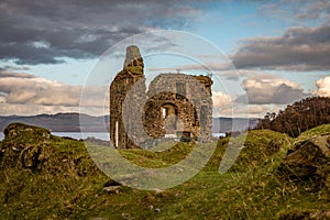 Sunset behind Castle Tarbert in the middle of the picture with rough lumpy rolling grass and rocks in the foreground