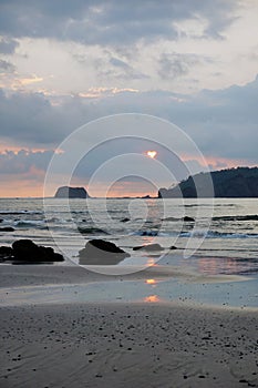 Sunset behind clouds reflecting on the beach
