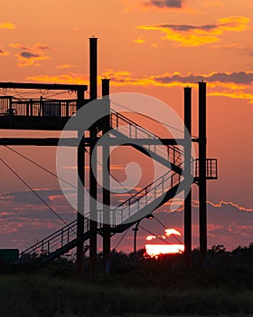 Sunset behind a silhouette of a staircase and zip line towers.