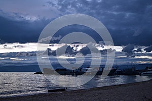 sunset with blue dark clouds in sky in bay of lake Baikal with jetty pier with old ships and boats, evening sea, reflection