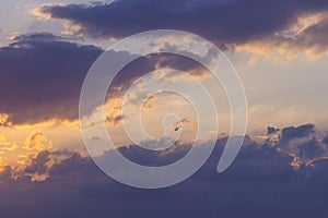 Sunset on a blue sky background - golden rays of the sun, dark-pink clouds and a flying helicopter