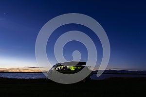 Sunset blue sky and camper van silhouette on the beach near the sea. Free parking and traveling through beautiful landscape -