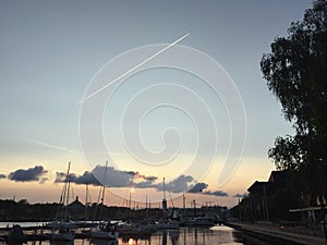 Sunset, boat, dock, plane and condensation trail.