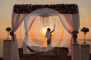 Sunset. bride silhouette. Wedding ceremony arch with flower arrangement with white curtain, outdoor photo. decor.