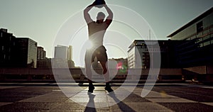 Sunset, city and a man with a slam ball for fitness, training or workout as a strong bodybuilder. Exercise, silhouette