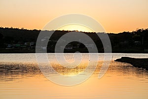 Sunset between clouds at dusk with golden sky, with reflection in pond.