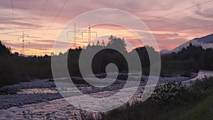 Sunset clouds over forest near river, silhouettes of electric power pylons and cables in distance