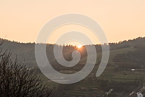 Sunset with colorful sky above forest in rural landscape witth fields, forest and small hills