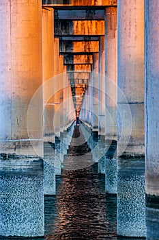 Sunset between columns that form the base of a bridge on the sea