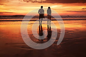 Sunset Couple. Silhouettes Of Young Man And Woman Staying Together At Beach. Vacation Or Honeymoon Concept.