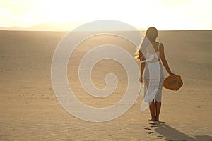 Sunset in the desert. Young woman with white dress walking in the desert dunes with footsteps in the sand during sunset. Girl