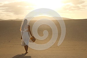 Sunset in the desert. Young woman with white dress walking in the desert dunes with footsteps in the sand during sunset. Girl