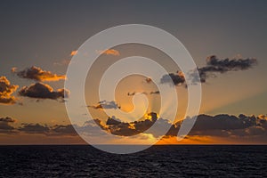 Sunset and dramatic set of clouds drifting over the tropical waters of the Caribbean Sea are lit by the last moments of daylight.