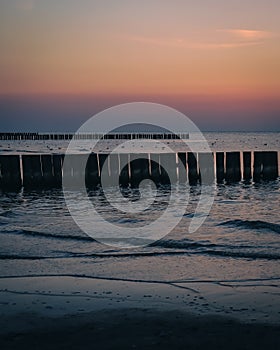 Sunset on an empty beach with wooden breakwaters.