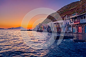 Sunset in fishermen village of Klima, Milos island, Greece. Pair of adults enjoy sunset view on pier of small