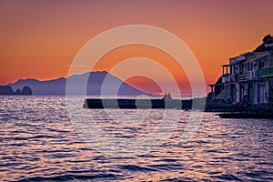Sunset in fishermen village of Klima, Milos island, Greece. Pair of adults enjoy sunset view on pier of small