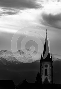 Sunset in a foggy mystic scenery with clouds and a mountain silhouette with a church tower in the austrian alps