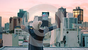 Sunset, freedom and a woman on city rooftop looking at skyline or cityscape. Winner, evening and zen, happy girl on roof