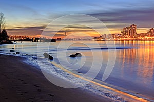 Sunset glow and city lights reflecting over river water and beach