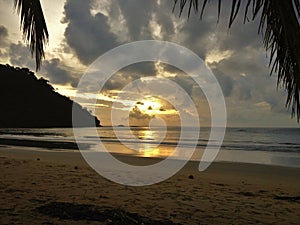 Sunset glow over a beautiful tropical beach and ocean water. Different colours of clouds and the silhouette of palm tree.